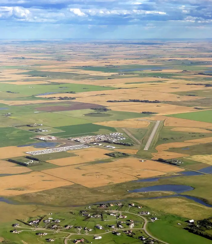 Green and gold fields, ponds and big acreage lawns near Airdrie from the air, the kind of yards that need the best landscaper in Airdrie