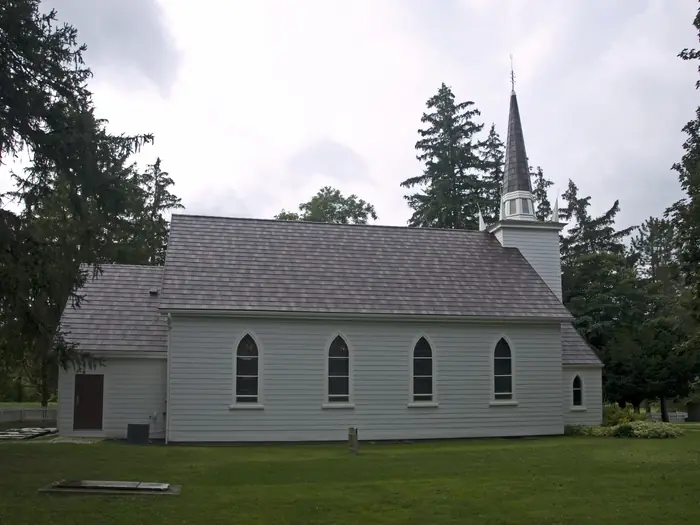 The white wooden Mohawk Chapel in Brantford, with a mowed lawn and tall evergreens