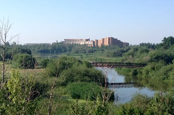 A footbridge over the water in Muskoseepi Park, with a college building behind