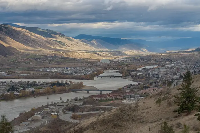 Kamloops and the Thompson River seen from a dry hillside, with bridges and brown hills behind