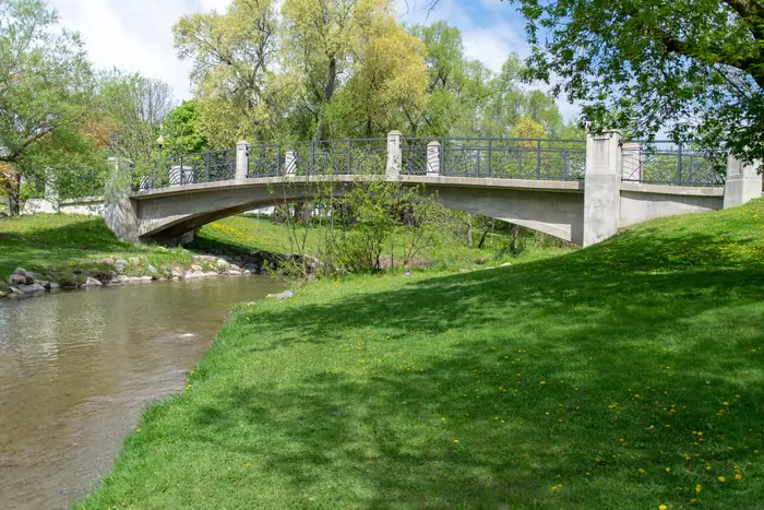 A footbridge and mowed grass banks along the creek at the Oshawa Valley Botanical Gardens in spring
