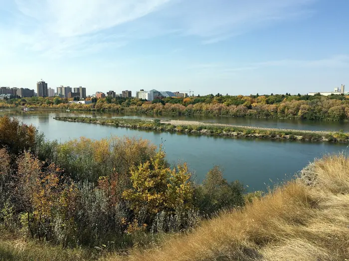 Dry prairie grass and fall shrubs on a slope above the river, with downtown Saskatoon in the distance