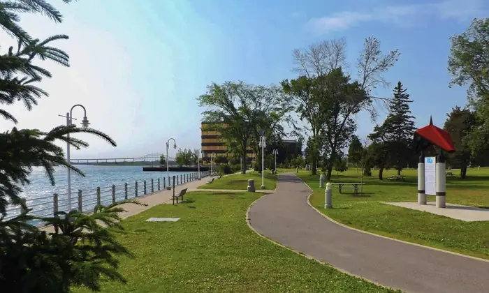 Mowed grass and a paved path beside the St. Marys River in Clergue Park, Sault Ste. Marie