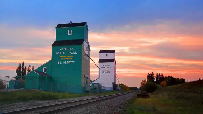 Two tall grain elevators marked St. Albert beside the train tracks at sunset