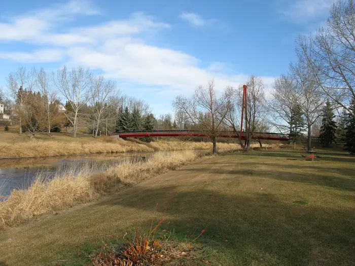 Mowed parkland and a red footbridge by the Sturgeon River before spring green-up, the kind of big lawn people hire the best landscaper in St. Albert for